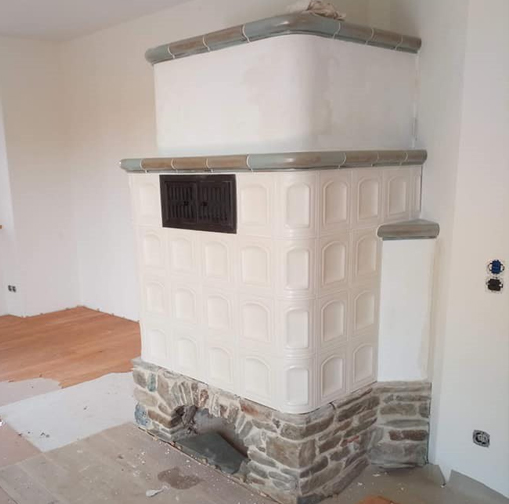 Warmluft- Speicherofen mit weißen Kacheln und Natursteinsockel