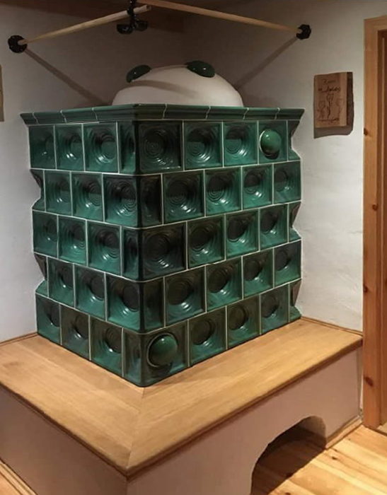 grüner wassergeführter Kachelofen mit Holzbank